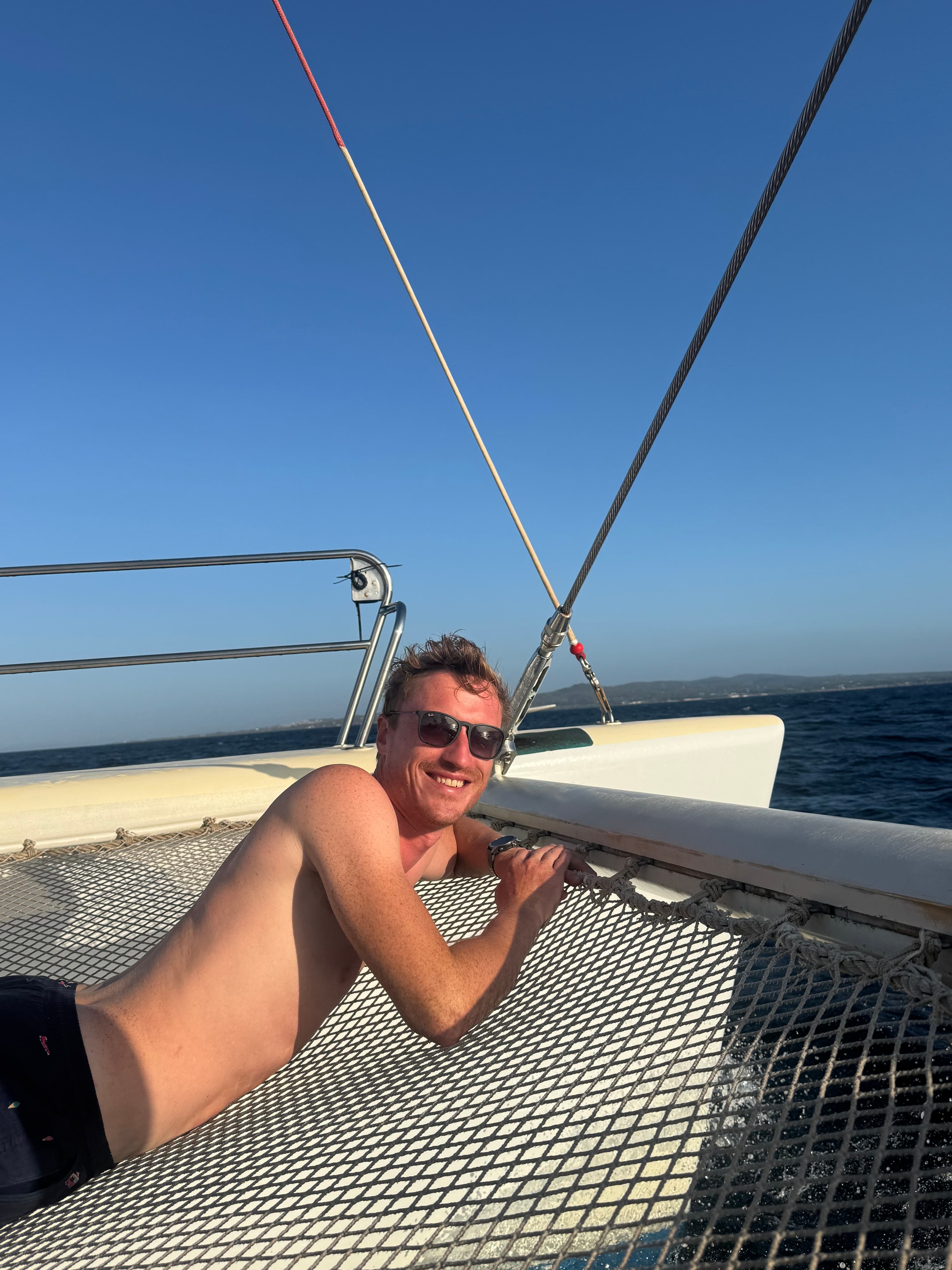 Jochen Jo co-founder relaxing on catamaran netting with ocean background